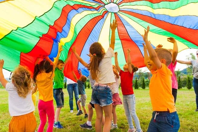 Barn som hoppar under en färgglad fallskärm i ett evenemang som organiseras med hjälp av Timely evenemangshanteringsprogramvara för festivaler.