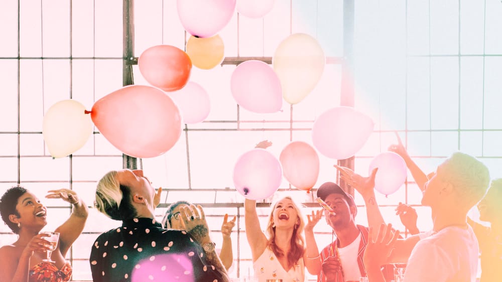A group of cheerful people celebrating and tossing pink and yellow balloons