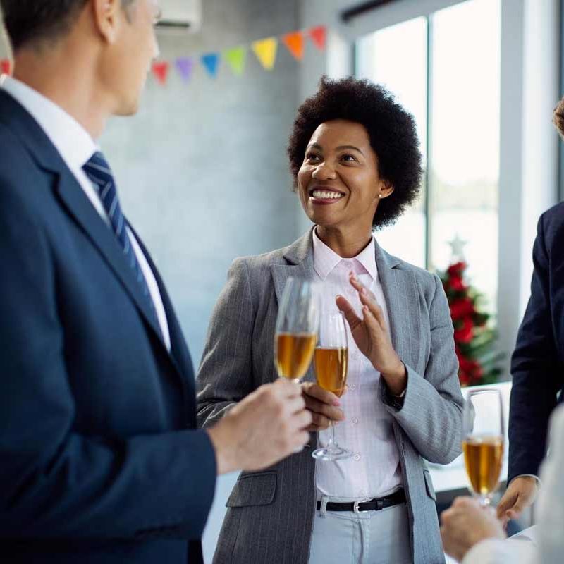 A professional woman and two colleagues at a happy hour meetup at the office holding  drinks.