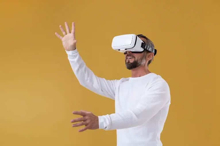 Älterer Mann trägt eine Augmented-Reality-Brille und greift mit beiden Händen nach oben und vorne.