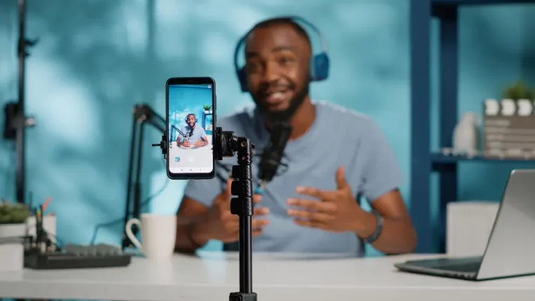 Un joven negro graba un video de Youtube en un teléfono inteligente con equipo de grabación de audio para usarlo como material para comercializar su programa de capacitación.