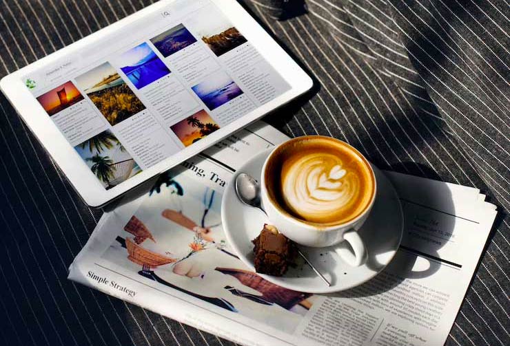 Beautiful cappuccino seating on top of a newspaper next to a tablet with different articles open 