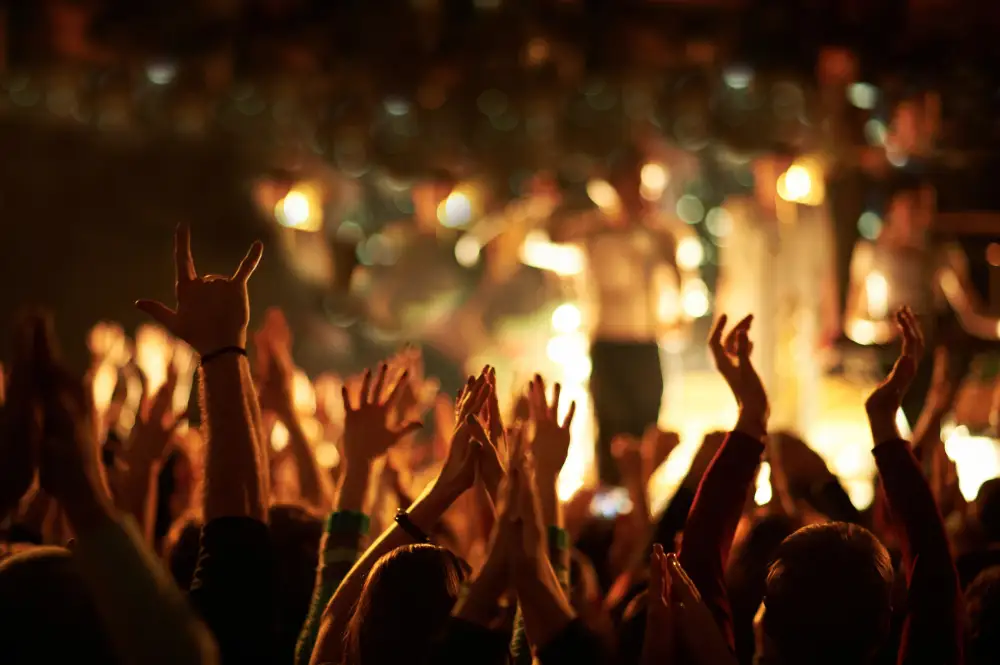 people at an outdoor music festival with their hands up celebrating.
