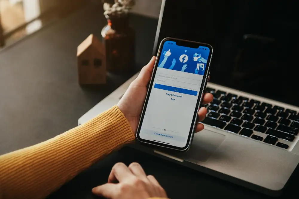 A woman holding up a smartphone showing the Facebook login page.