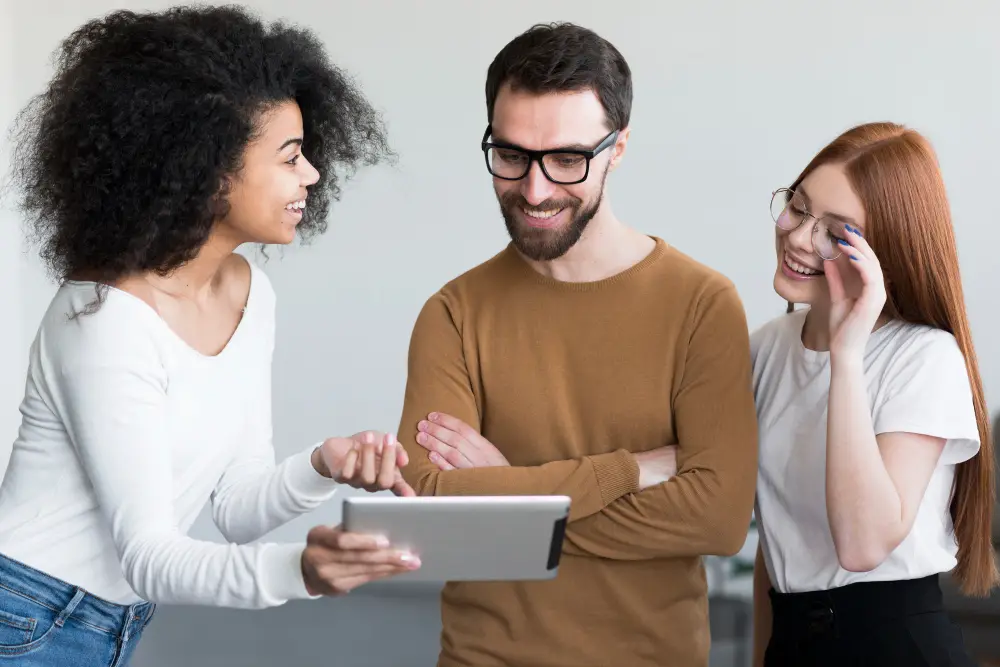 trois jeunes souriants et ayant une interaction animée tout en regardant une tablette.