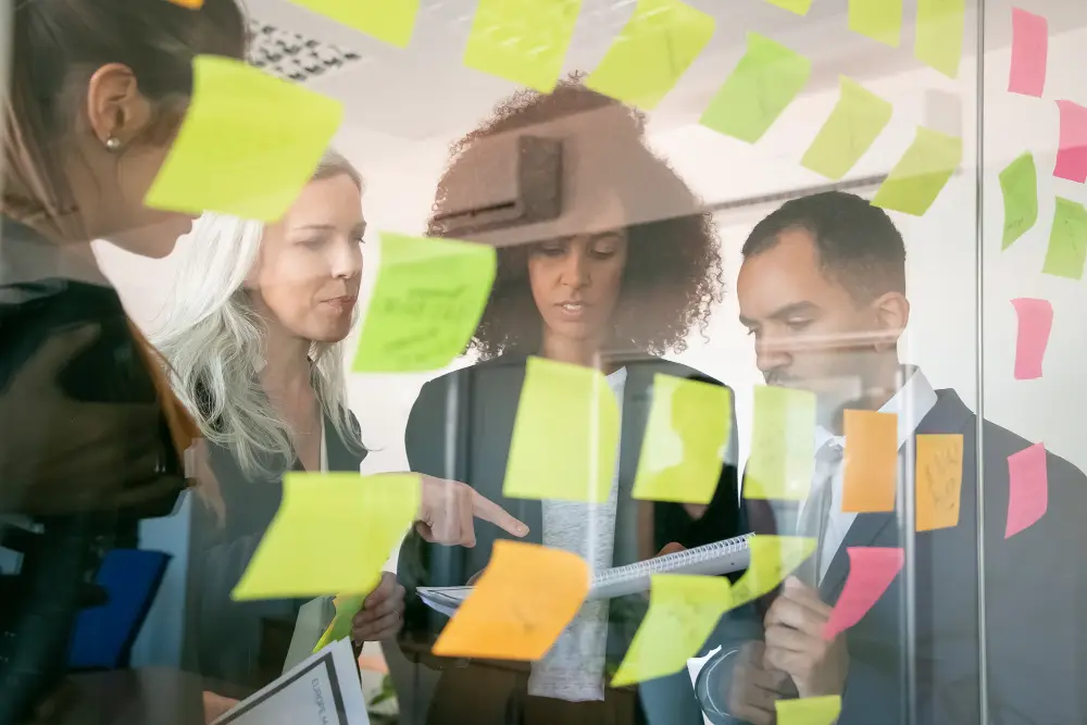 un groupe de personnes remue-méninges dans un bureau avec plusieurs notes autocollantes colorées.