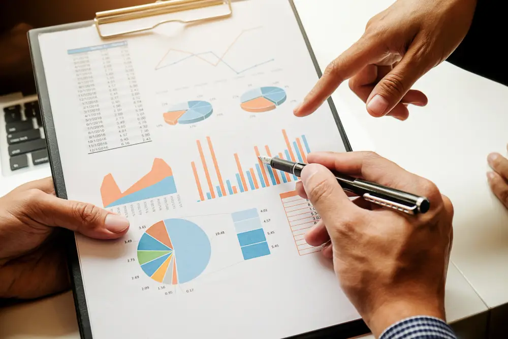 close-up shot of a professional report with charts and tables and two people's hands pointing to it.