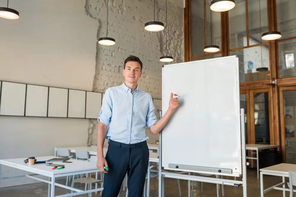 professional young man standing in an office room next to a whiteboard with a marker on his hand.