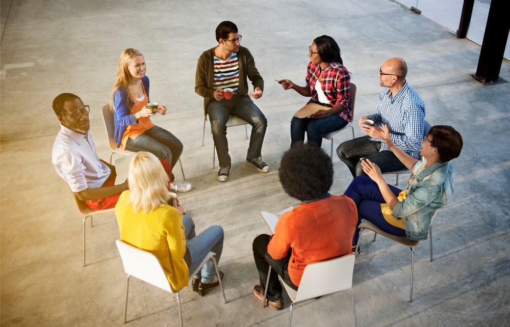 A mixed group of people seated in a circle, talking and exchanging ideas, to symbolize the power of utilizing Facebook groups.