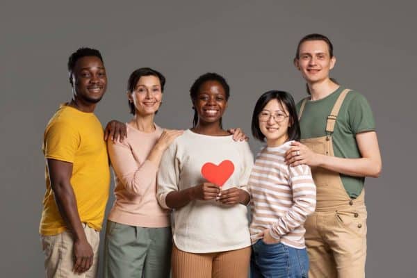 Une équipe diversifiée d'organisateurs à but non lucratif célébrant l'acquisition Timelyavec la nouvelle réduction de 15 % pour les organisations à but non lucratif, tenant un cœur en papier pour présenter leur cause sociale.