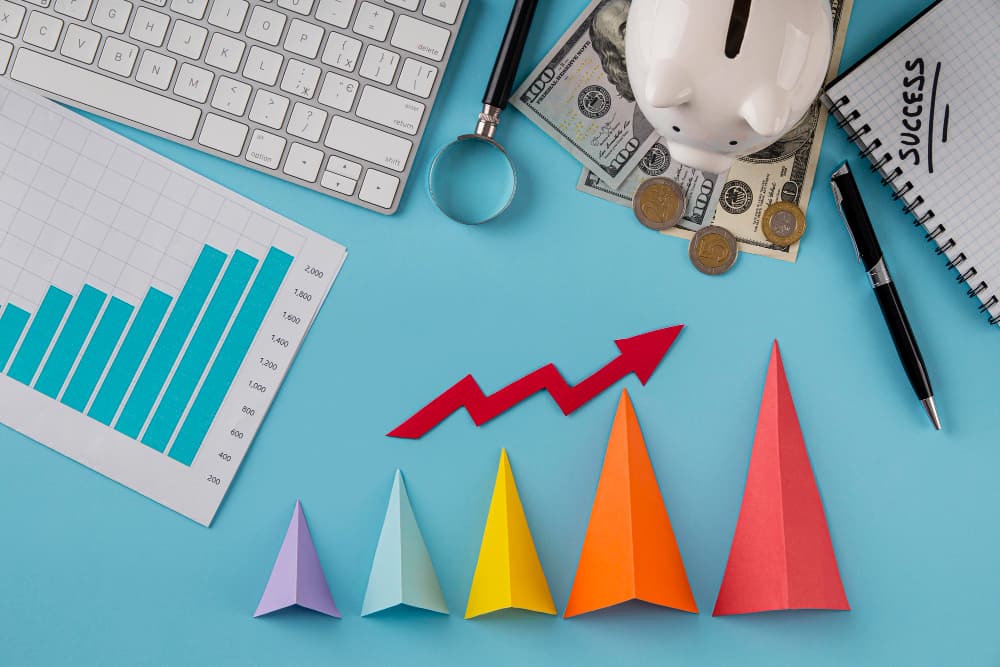 a table with several elements, money, an upward arrow, a graph, a notebook with the word success written on it, representing the benefits of blended learning for training professionals.