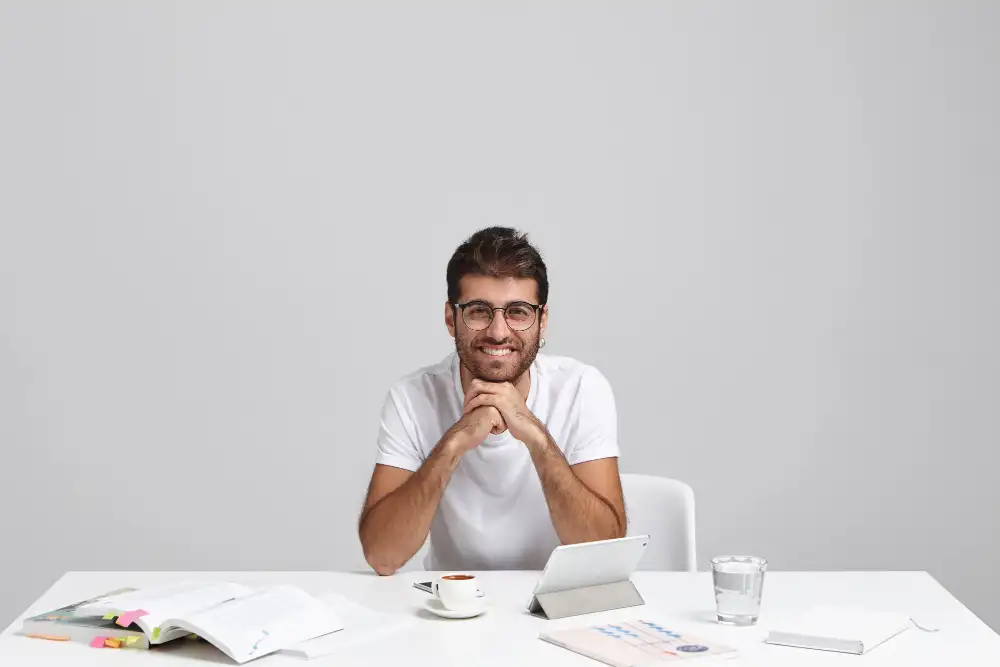 a young marketing professional sitting with his elbows on a desk, smiling as he explains ways to sell online courses from your own website. 