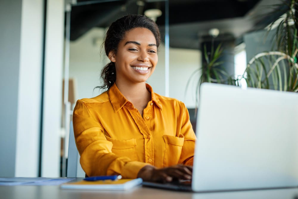 professional young black woman wearing a yellow shirt, updating her events calendar on her laptop