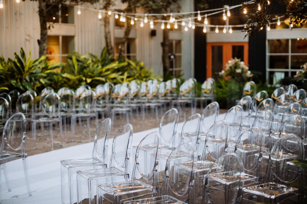A beautiful outdoor venue seating area with transparent chairs and string lights. 