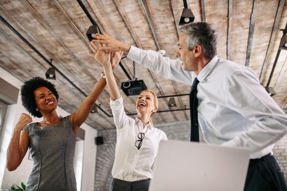 A team of professionals celebrating and high-fiving at an office.