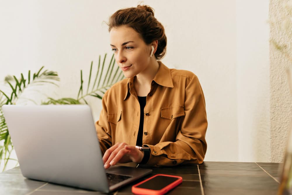 Een jonge professionele vrouw die een karameloverhemd draagt ​​en op een laptop werkt.