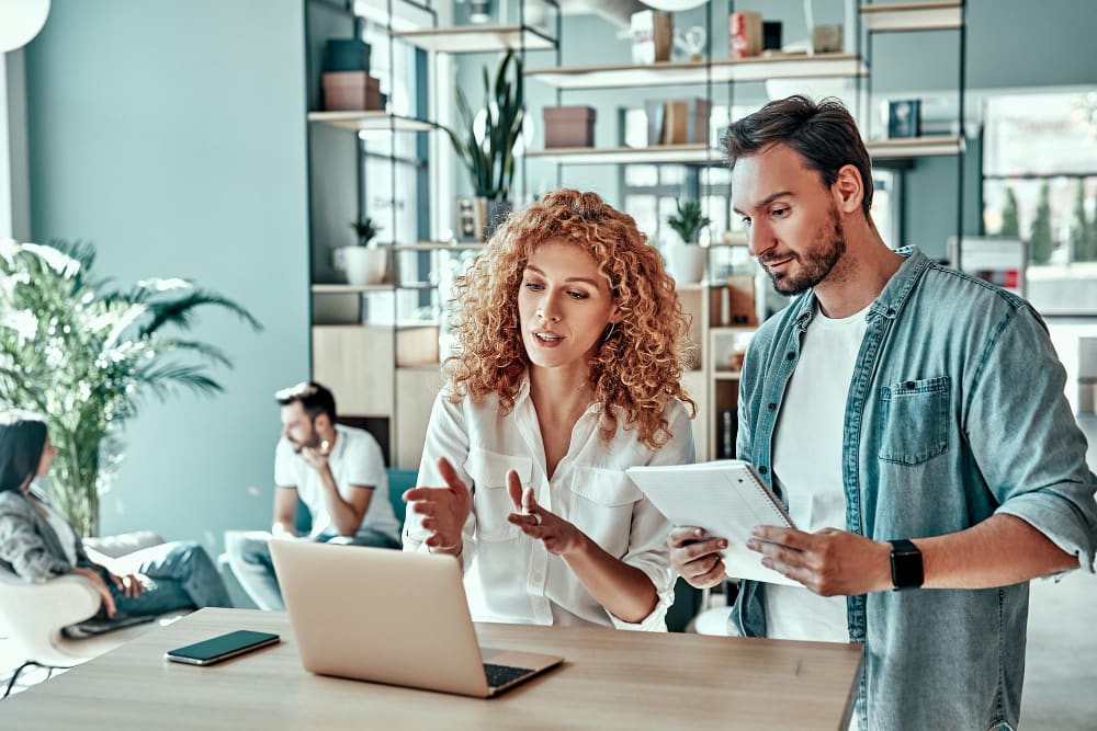 twee collega's bespreken strategieën voor evenementenbeheer en kijken naar een laptop.