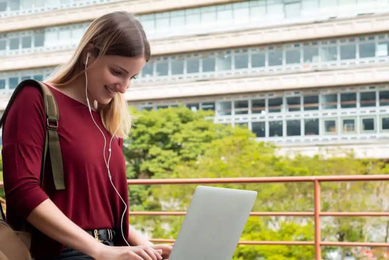 giovane studentessa di istruzione superiore sul suo laptop con auricolari nell'utilizzo di strumenti di intelligenza artificiale.