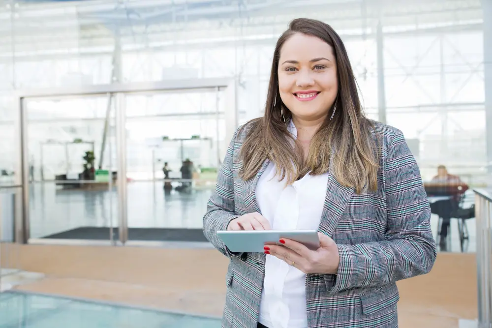 Femme habillée de manière professionnelle avec un costume gris, tenant une tablette avec ses recherches sur les meilleures applications pour la planification d'événements.