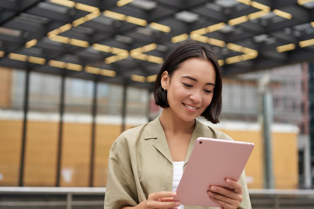 Une jeune femme asiatique utilisant une tablette avec un étui rose.