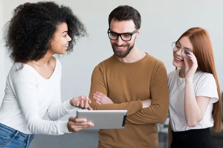 três jovens sorrindo e tendo uma interação animada enquanto olham para um tablet.
