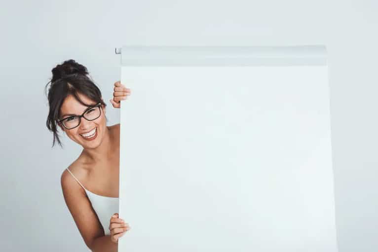 mulher profissional sorrindo, enfiando a cabeça de brincadeira atrás de um quadro branco.