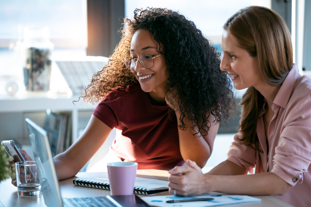 Dos mujeres mirando juntas una computadora portátil y sonriendo.