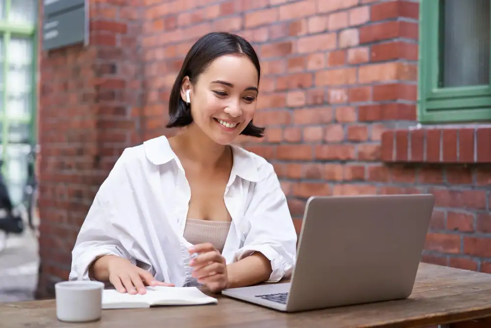 Young woman browsing on a laptop and writing on a journal.