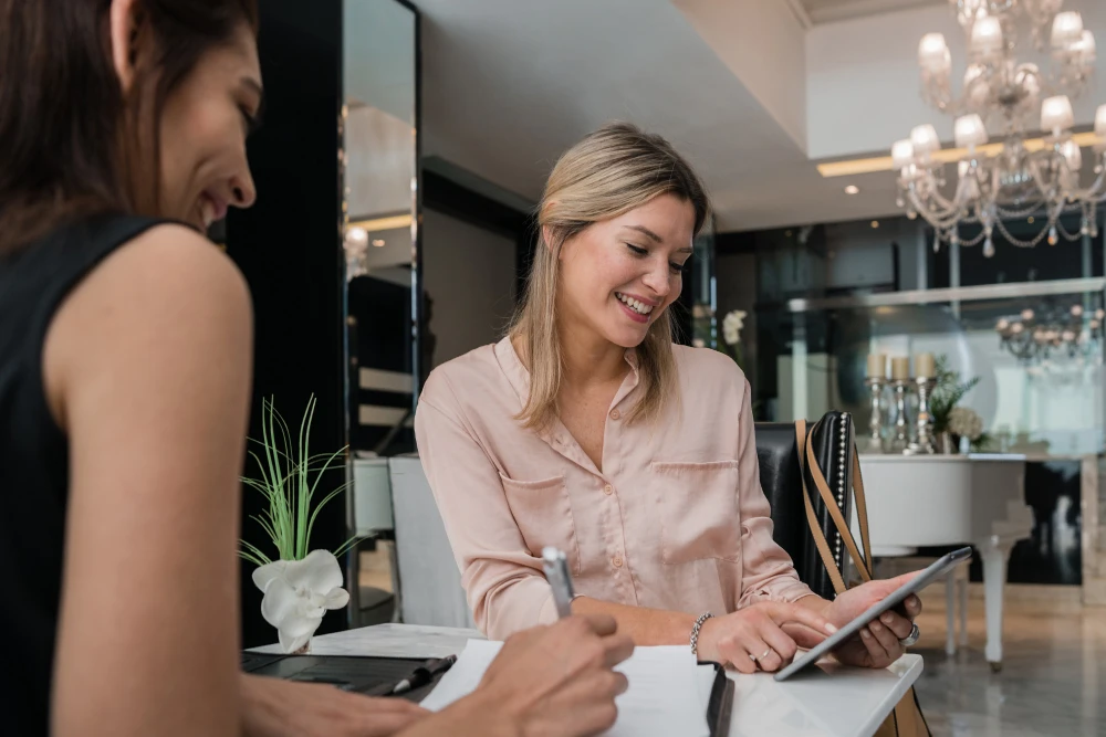 Two women having a lively conversation while using a tablet, at a beautiful venue.